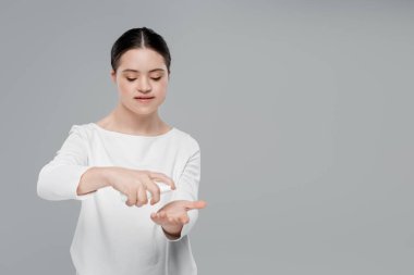 Down sendromlu genç bir kadın el dezenfektanı uyguluyor. Griye izole edilmiş. 