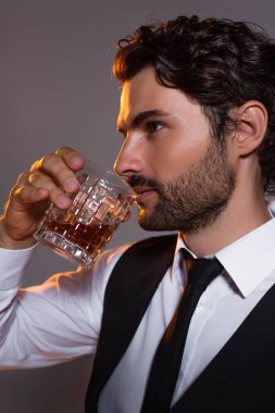 Beyaz gömlekli esmer adam ve siyah kravatlı. Gri üzerine izole edilmiş viski içiyor.