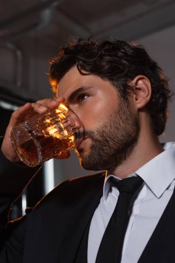 Gri arka planda viski içen şık sakallı adam.