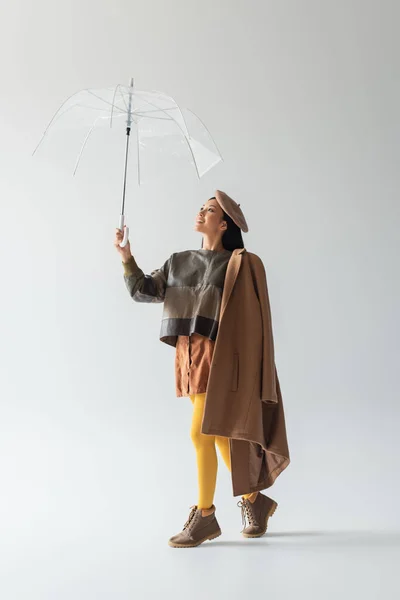 グレーの透明傘の下で革のプルオーバーと黄色のタイツでアジアの女性の完全な長さビュー — ストック写真