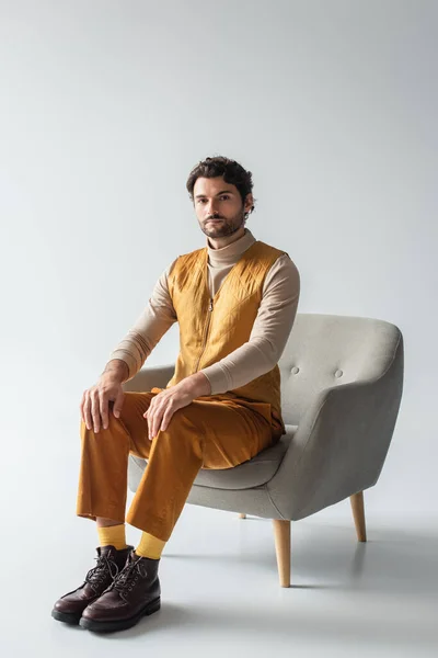 身穿黄色背心和长裤的男子坐在灰色扶手椅上的全景 — 图库照片
