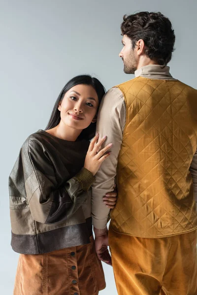 Счастливая Азиатка Кожаном Пуловере Опирающаяся Мужчину Желтом Жилете Изолированном Сером — стоковое фото