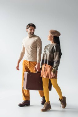 Irklar arası modaya uygun bir çift klasik bavul taşıyor ve gri renkte birbirlerine gülümsüyorlar.