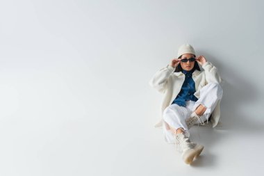 Gri üzerinde otururken Asyalı bir kadının güneş gözlüğünü ayarlarken yüksek açılı görüntüsü