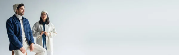 Азиатка Белой Куртке Шапочке Рядом Стильный Мужчина Сидит Изолированный Сером — стоковое фото