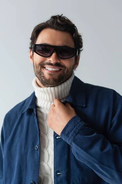 Uśmiechnięty Mężczyzna Niebieskiej Kurtce Ciemnych Okularach Przeciwsłonecznych Odizolowany Szaro — Zdjęcie stockowe