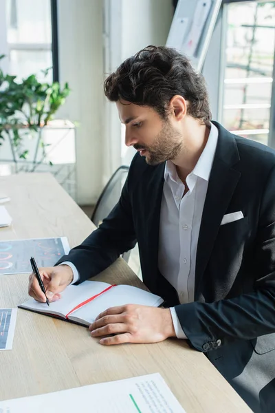 Homem Negócios Elegante Escrevendo Caderno Vazio Perto Papéis Mesa Escritório — Fotografia de Stock