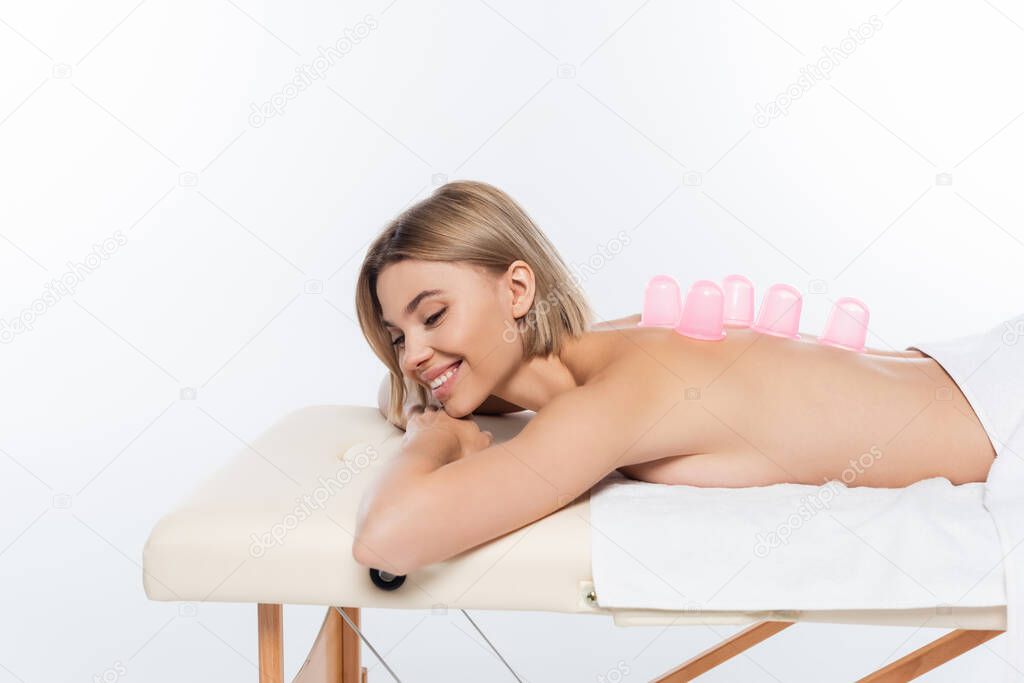 happy young woman with pink massage cups on back lying on massage table on white