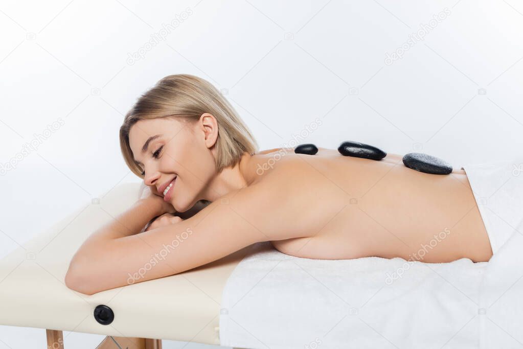 pleased young woman receiving hot stone massage on white