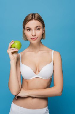 Sarışın, beyaz sütyenli, olgun, yeşil elmalı, mavi renkli bir kadın. 
