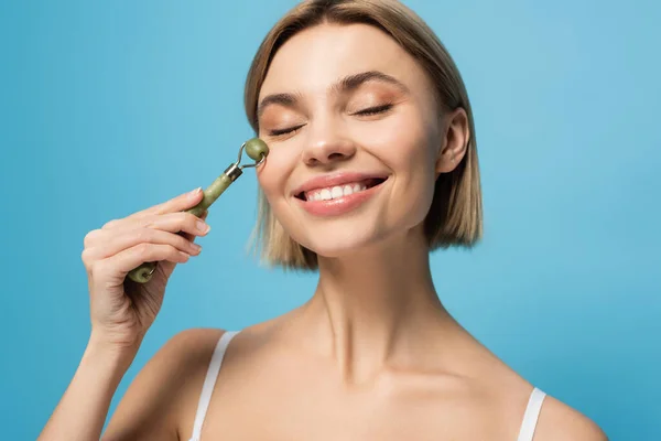 Cheerful Young Woman Massaging Face Jade Roller Isolated Blue — Stock Photo, Image