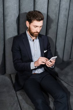 Resmi kıyafetli sakallı adam otel lobisinde akıllı telefon kullanıyor. 