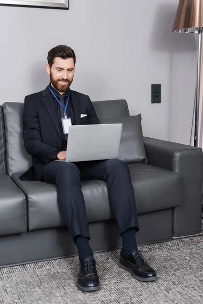 Cheerful Businessman Badge Using Laptop While Sitting Leather Couch Hotel — Stock Photo, Image