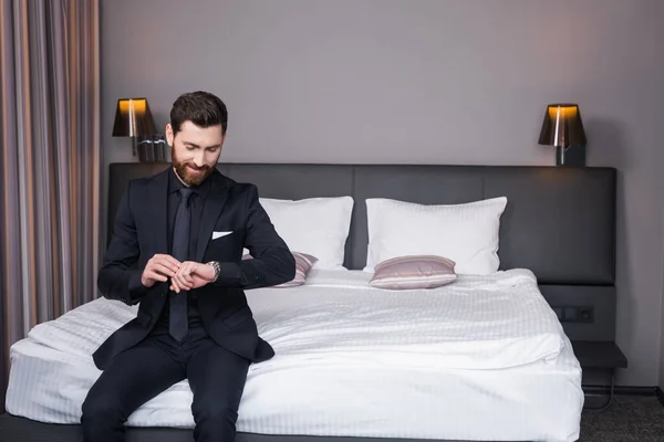 Homem Alegre Terno Verificando Tempo Enquanto Sentado Cama Quarto Hotel — Fotografia de Stock