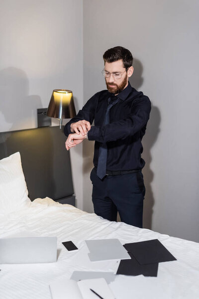 bearded man in eyeglasses adjusting wristwatch in hotel