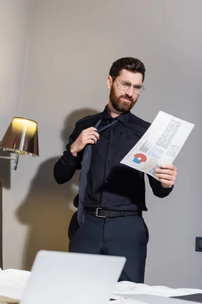 Skäggig Man Glasögon Justera Slips Och Titta Infographics Hotellet — Stockfoto