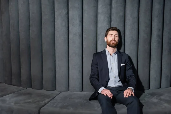 businessman in earphones and suit sitting with closed eyes in hotel foyer