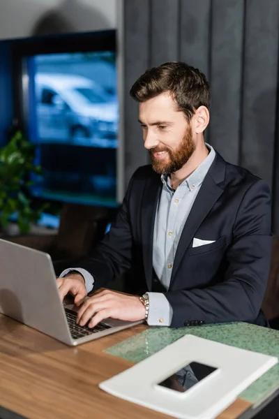 Homem Alegre Terno Digitando Teclado Laptop Perto Celular Lobby Hotel — Fotografia de Stock