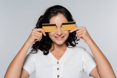 Gri, nakit para kavramına izole edilmiş kredi kartlarıyla gözlerini kapatan mutlu genç bir kadın.