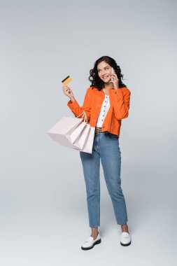 Elinde nakit para ve gri alışveriş torbalarıyla elinde kredi kartıyla akıllı telefondan konuşan mutlu bir kadın.