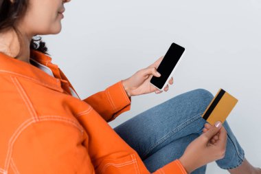 Beyaz ekran ve kredi kartı gri üzerinde izole edilmiş akıllı telefon kullanan kadın görüntüsü