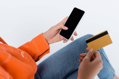 Beyaz ekran ve kredi kartlı akıllı telefonu gri renkte tutan kadının kırpılmış görüntüsü