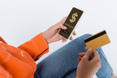 partial view of woman holding smartphone with cashback on screen and credit card isolated on grey  clipart