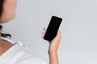 Gri ekranda boş ekranlı cep telefonu tutan kadının kırpılmış görüntüsü