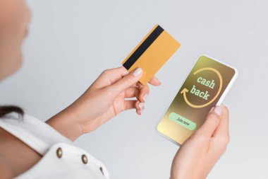 Ekranda nakit para ve gri renkli kredi kartı olan cep telefonu tutan kadının kısmi görüntüsü 