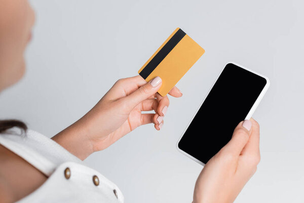 обрезанный вид женщины, держащей мобильный телефон с чистым экраном и кредитной картой, изолированной на сером