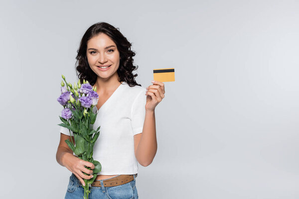 счастливая женщина держит букет цветов и кредитную карту изолированы на серый 