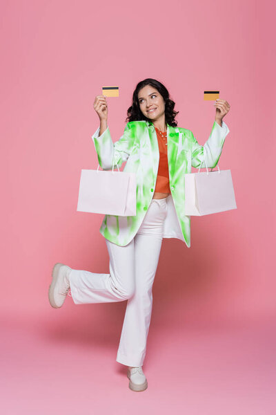 полная длина счастливая молодая женщина в галстук краситель для галстука держа кредитные карты и сумки на розовый 