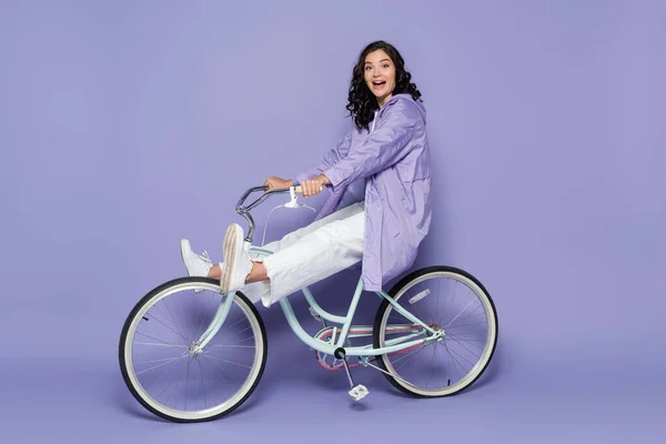 全身上下都是穿着紫色雨衣骑自行车的令人惊讶的年轻女子 — 图库照片