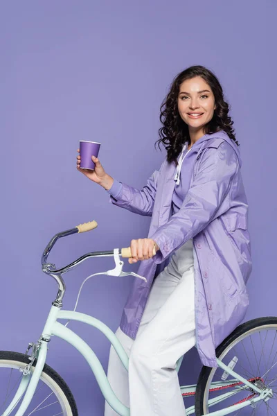Feliz Jovem Mulher Capa Chuva Violeta Andar Bicicleta Segurando Copo — Fotografia de Stock