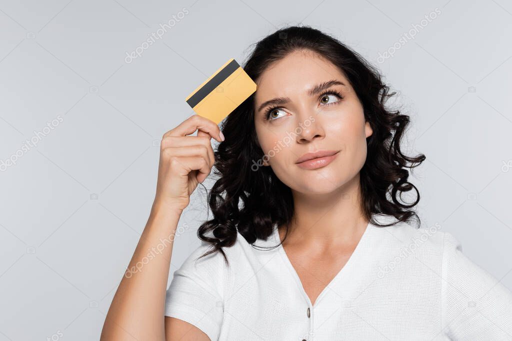 pensive young woman holding credit card with cashback isolated on grey