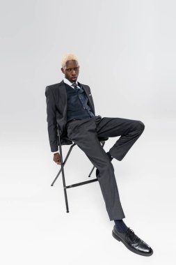 Resmi olarak sarışın ve genç Afrikalı Amerikalı bir adam gri sandalyede oturuyor.