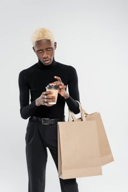 Gri üzerinde izole edilmiş poşetler ve kağıt bardaklarla duran şık Afrikalı Amerikalı adam. 