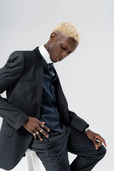 blonde african american man in suit leaning on chair isolated on grey