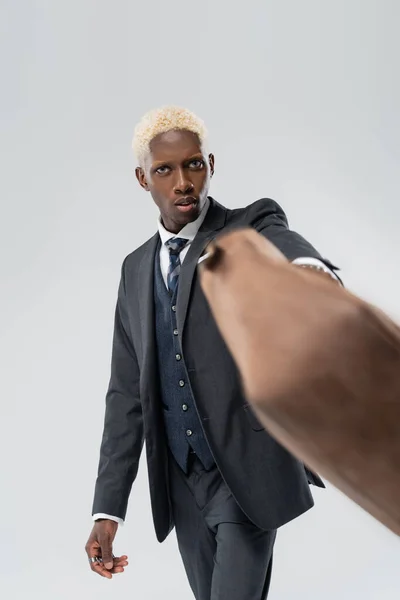 blonde african american man in suit holding blurred leather bag isolated on grey