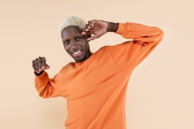 Turuncu kazaklı mutlu Afro-Amerikan adam bej renkli kameraya bakıyor. 