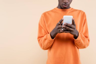Turuncu kazaklı Afro-Amerikan bir adamın bej üzerine izole edilmiş akıllı telefon kullanması. 