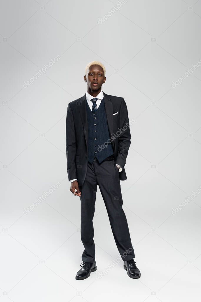 full length of elegant african american man in formal wear standing with hand in pocket on grey