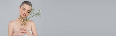 young woman with closed eyes posing with white tiny flowers isolated on grey, banner clipart