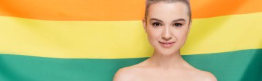 woman with naked shoulders smiling at camera near lgbt flag on background, banner clipart
