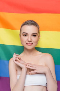 Arka planda lgbt bayrağı yakınındaki kameraya gülümseyen beyaz elbiseli mutlu kadın.