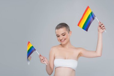 Beyaz bluzlu mutlu kadın gri üzerinde küçük Igbt bayraklarıyla poz veriyor.