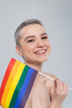 Gri üzerine izole edilmiş küçük lgbt bayrağı yakınında kameraya bakan heyecanlı kadın