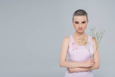 Göğüs kanseri olan genç bir kadın. Farkındalık kurdelesi ve gri renkli çingene çiçekleri.