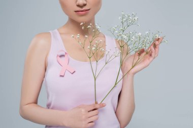 Pembe farkındalık kurdelesiyle poz veren kolsuz tişörtlü bir kadın ve gri renkli çingene çiçekleri.