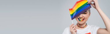 Gri pankartta izole edilmiş küçük LGBT bayrağıyla yüzünü gizleyen mutlu bir kadın.